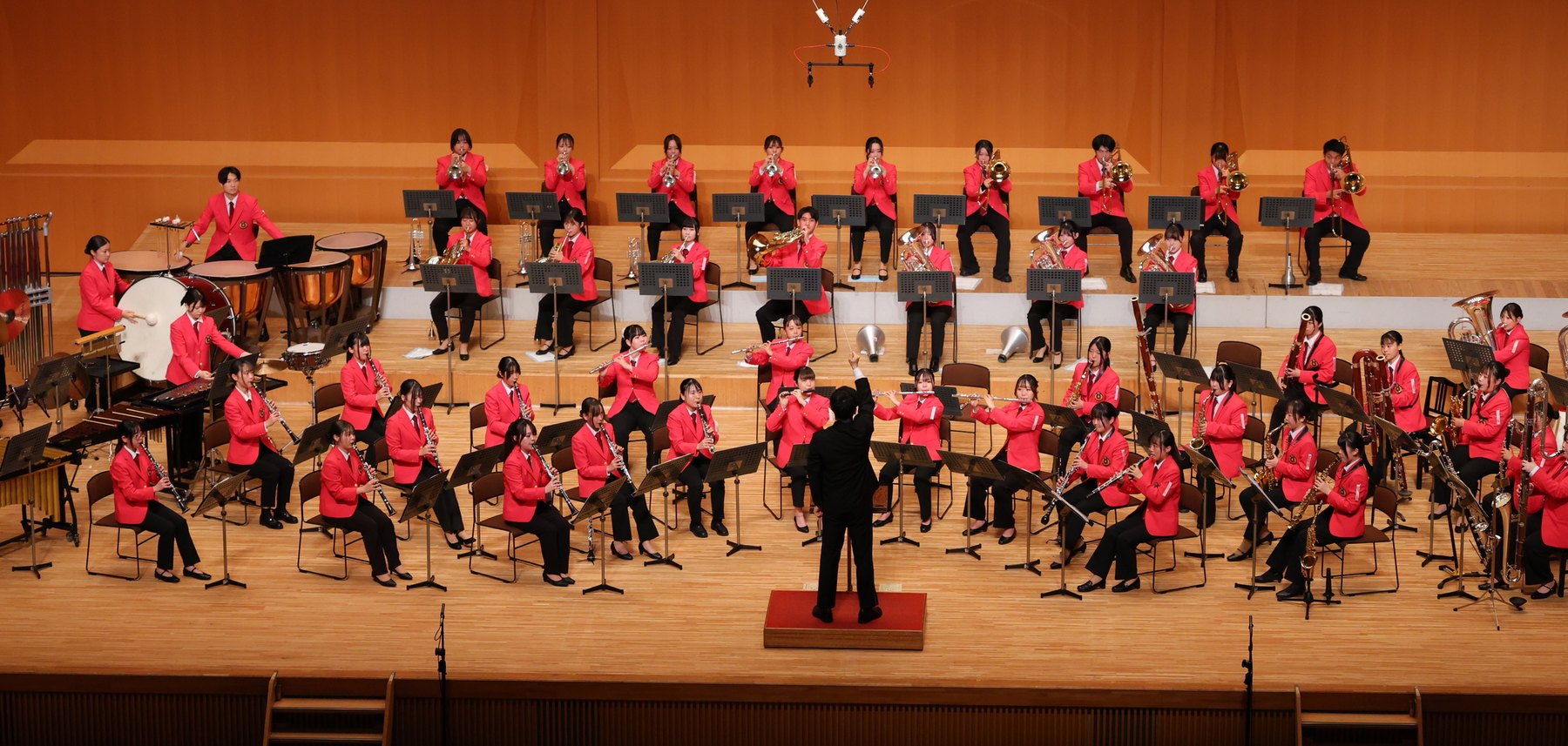 ホールのステージで指揮者とともに演奏する部員